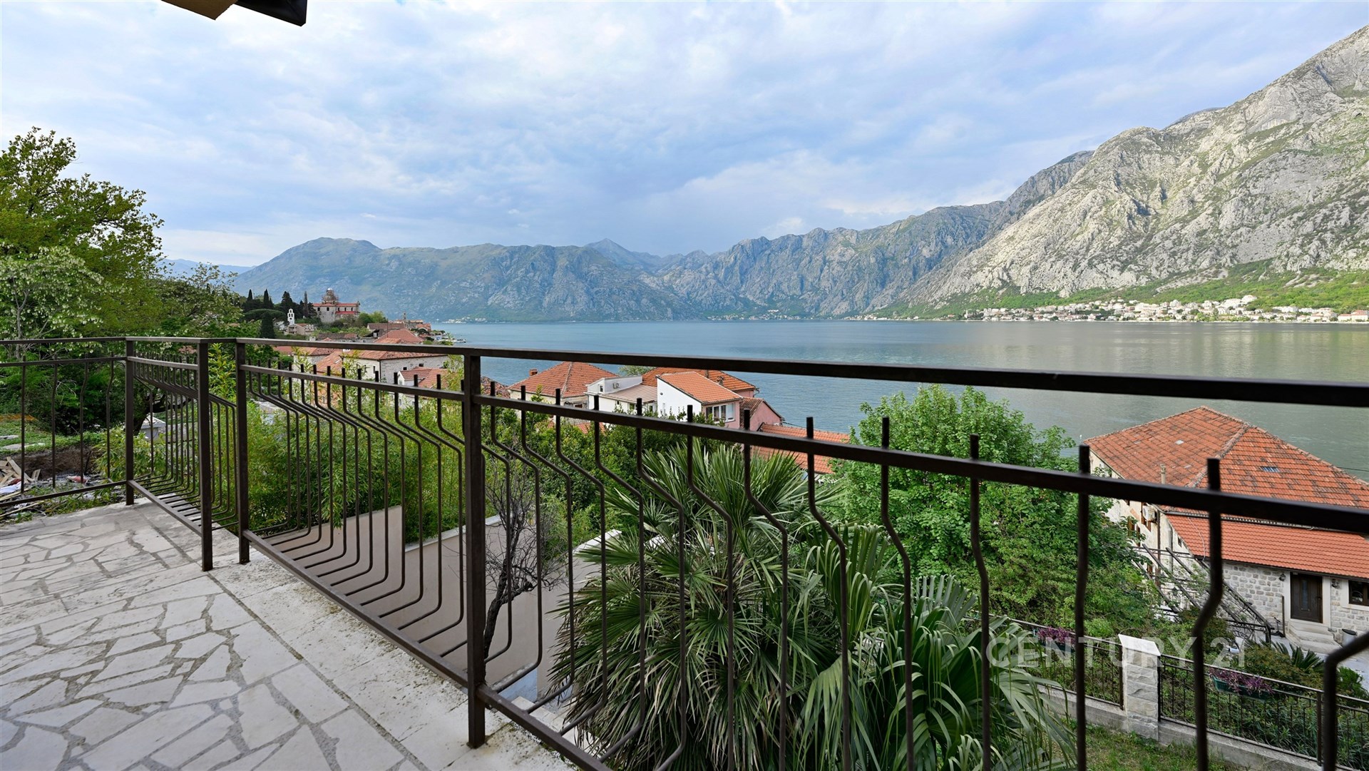 Výhled z terasy s kamennou dlažbou, kovové zábradlí, panoramatický výhled na moře a hory, ideální prosluněné místo pro relaxaci.