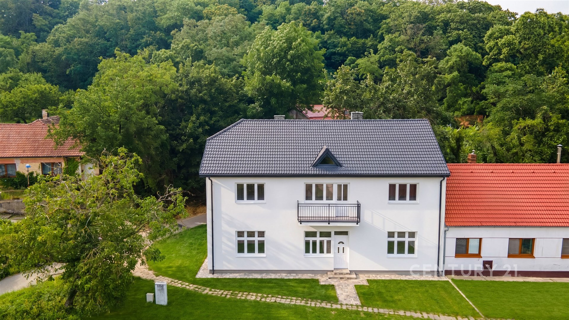 Velký rodinný dům s novou střešní krytinou a bílou fasádou, obklopený zelení. Klidná lokalita s velkou zahradou, vhodná k relaxaci.