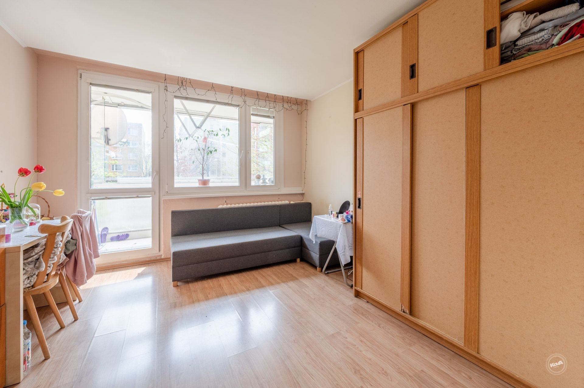 Světlý obývací pokoj s parketovou podlahou, velká okna s výhledem do zeleně a vstupem na balkon
