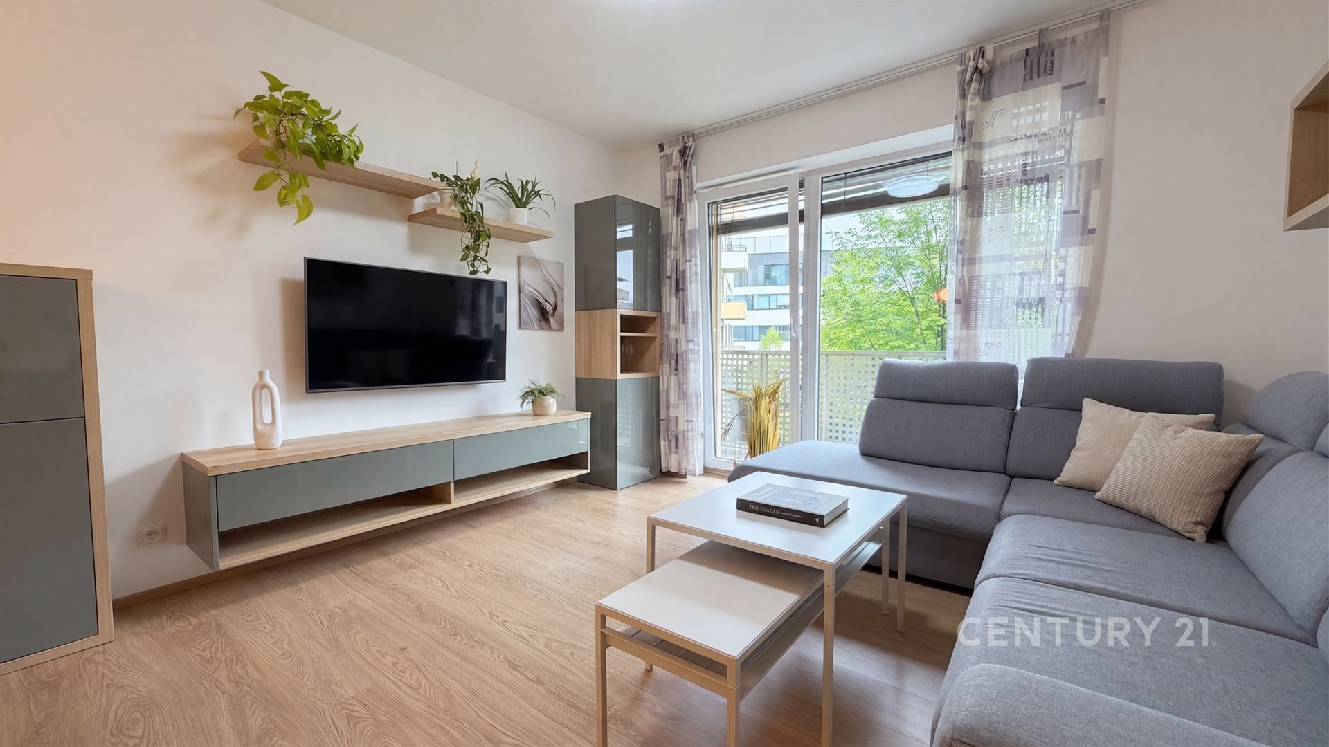 Světlý obývací pokoj s dřevěnou podlahou, velkými okny a moderním nábytkem.