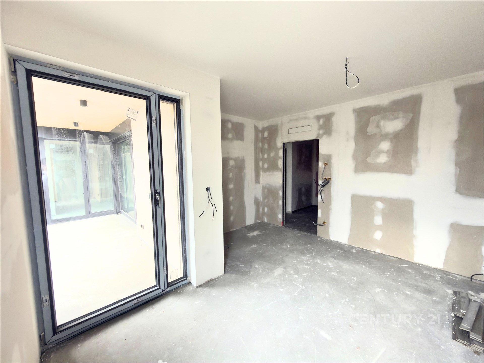 Prázdný pokoj s velkými okny, betonová podlaha, připraven k rekonstrukci, moderní dispozice, světlý interiér, vhodný pro úpravy.