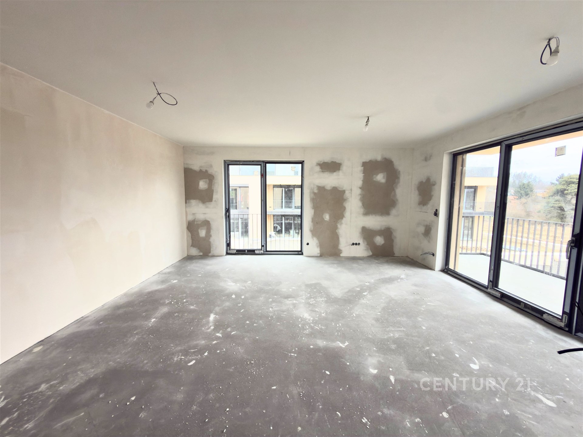 Prázdný obývací pokoj s velkými okny, betonovou podlahou a moderními prvky, připravený k dokončení nebo rekonstrukci.