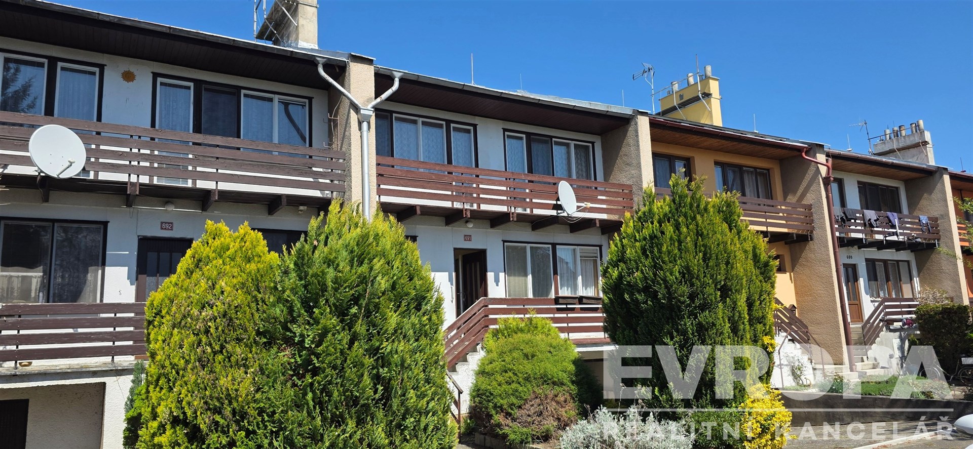 Řadový dům s dřevěnými balkony, předzahrádkou a satelitními parabolami, vhodný k rekonstrukci, nacházející se v klidné rezidenční čtvrti.