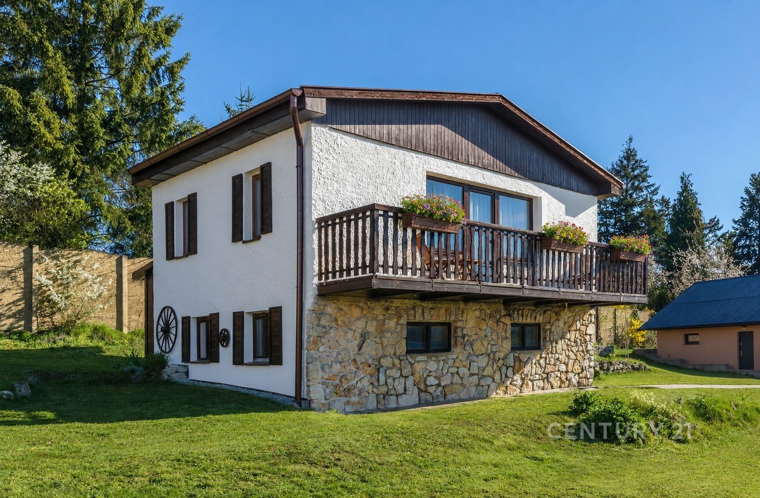 Dvoupatrový rodinný dům se zahradou, dřevěným balkonem a kamennou fasádou, situovaný v klidné přírodní lokalitě.