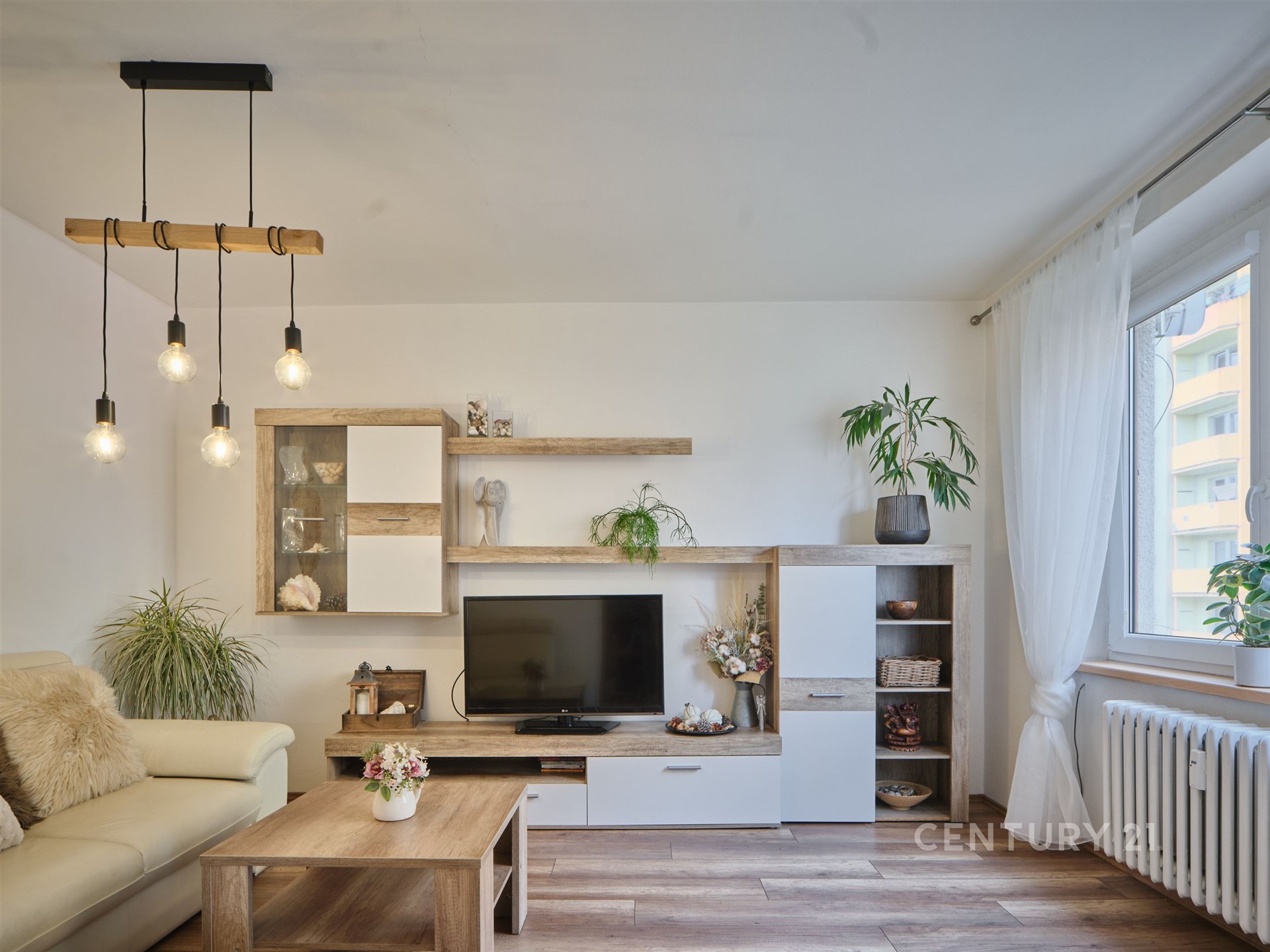 Světlý obývací pokoj s moderní parketovou podlahou, velkými okny a elegantním nábytkem ve světlém dřevě, vhodný pro komfortní bydlení.