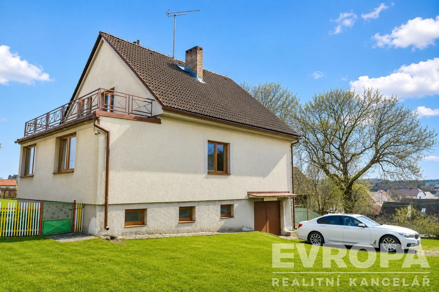 Rodinný dům s balkónem, dřevěnými okny a velkou zahradou. Nabízí dost prostoru, jasný výhled a klidné okolí, ideální pro rodinné bydlení.