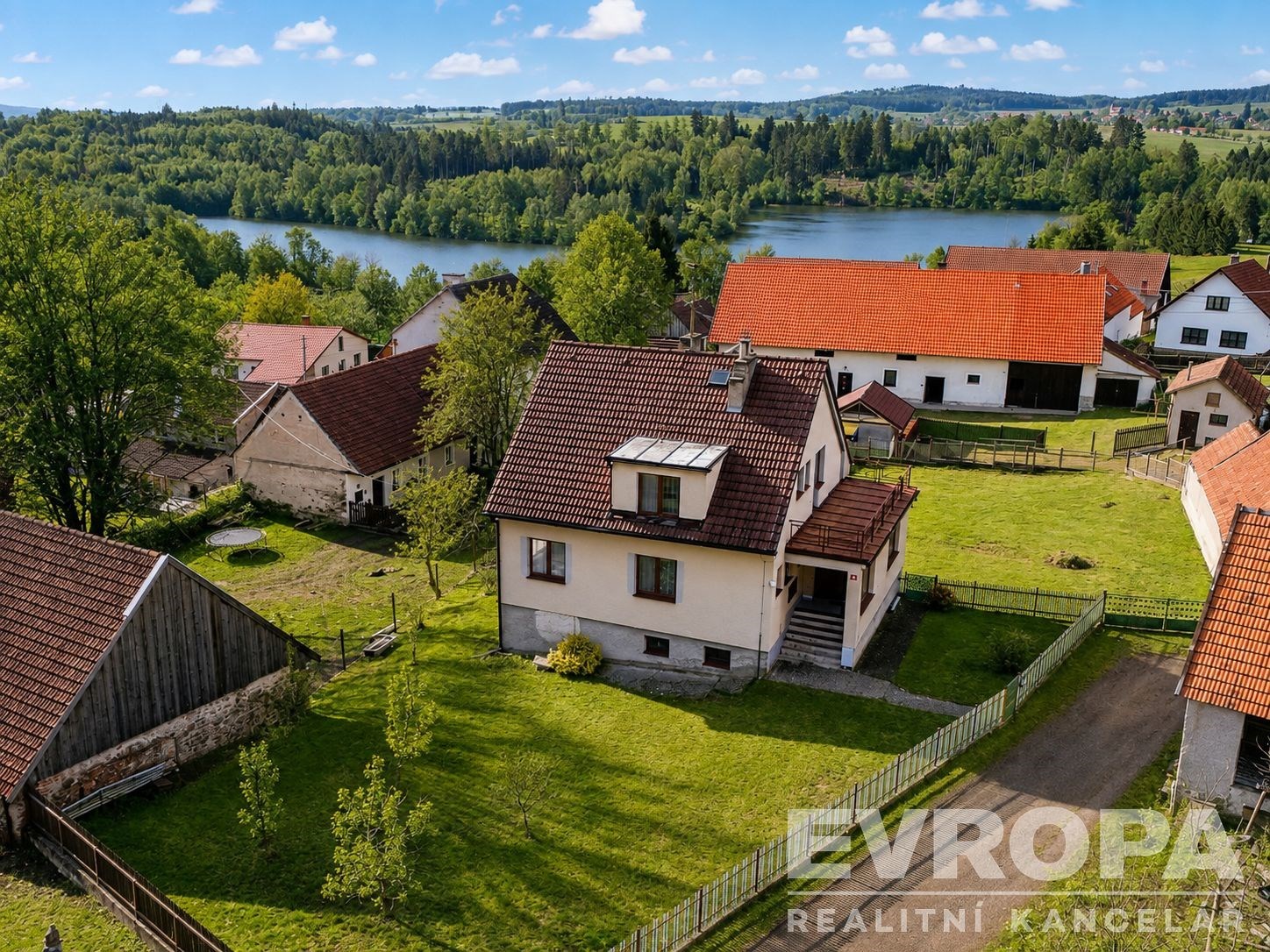 Rodinný dům s červenou střechou, obklopený rozsáhlou zahradou, nabízí klidné bydlení blízko přírody. Vhodné pro rodiny hledající klidný životní styl.