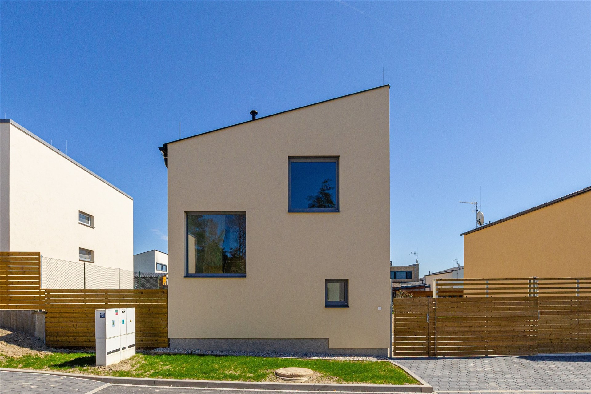 Moderní rodinný dům s velkými okny a dřevěným oplocením na klidném předměstí, energeticky úsporná stavba s minimalistickým designem