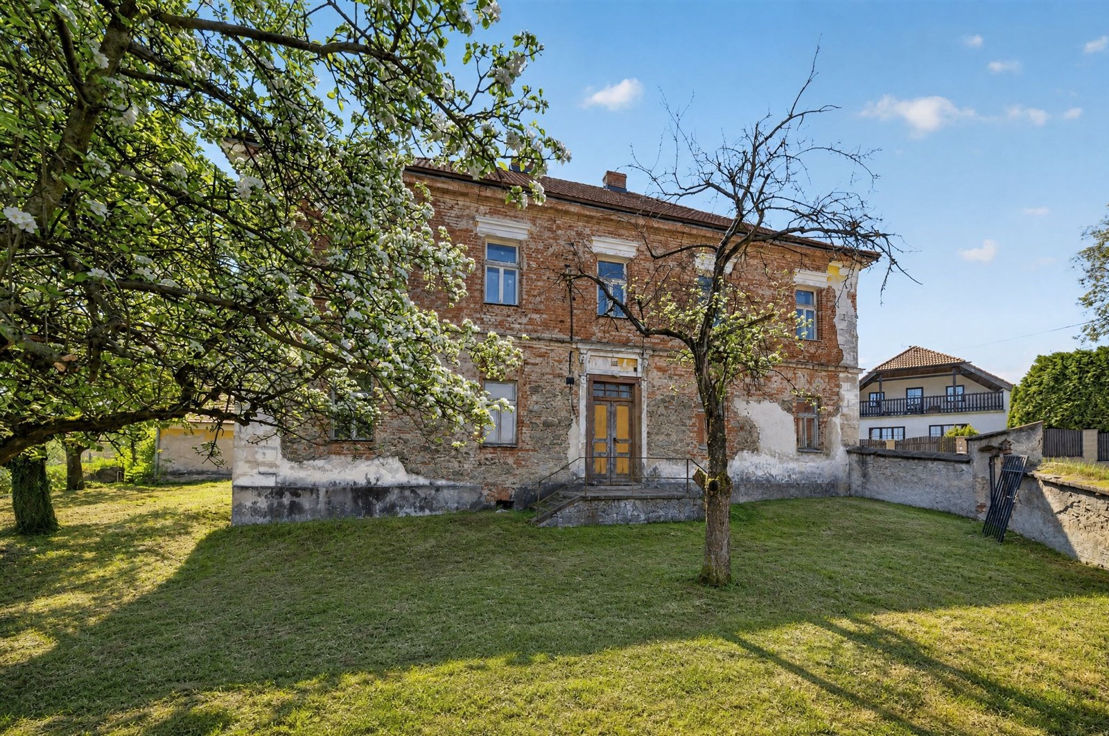Historická budova s cihlovou fasádou, velkou zahradou a šikmou střechou, nabízí potenciál pro renovaci v klidné lokalitě.