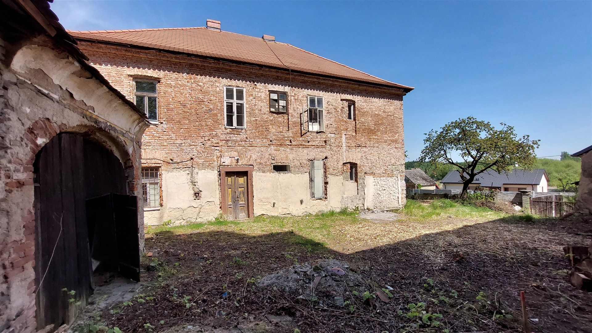 Velký venkovský dům s cihlovou fasádou a šikmou střechou, vyžadující rekonstrukci, obklopený rozlehlým pozemkem.