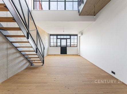 Světlý obývací pokoj s parketovou podlahou a velkými okny, moderní design s kovovým schodištěm a betonovým stropem. | Prodej bytu, 2+kk, 65 m²