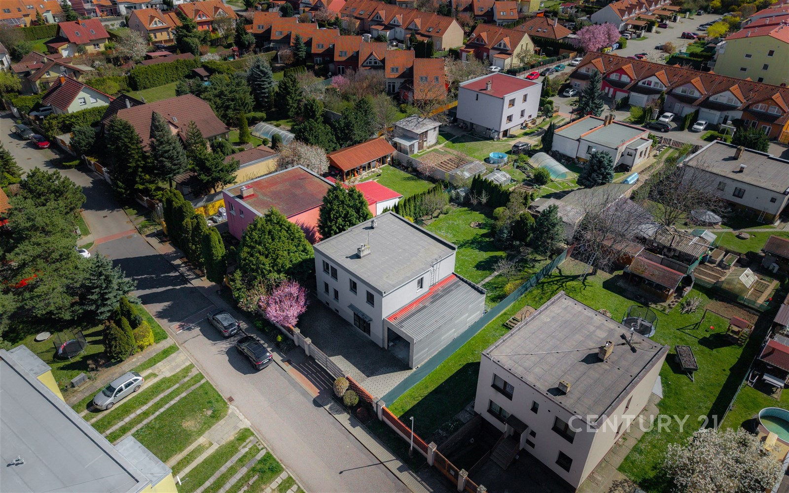 Letecký pohled na klidnou rezidenční čtvrť s moderními rodinnými domy, zahradami a dlážděnými příjezdovými cestami.