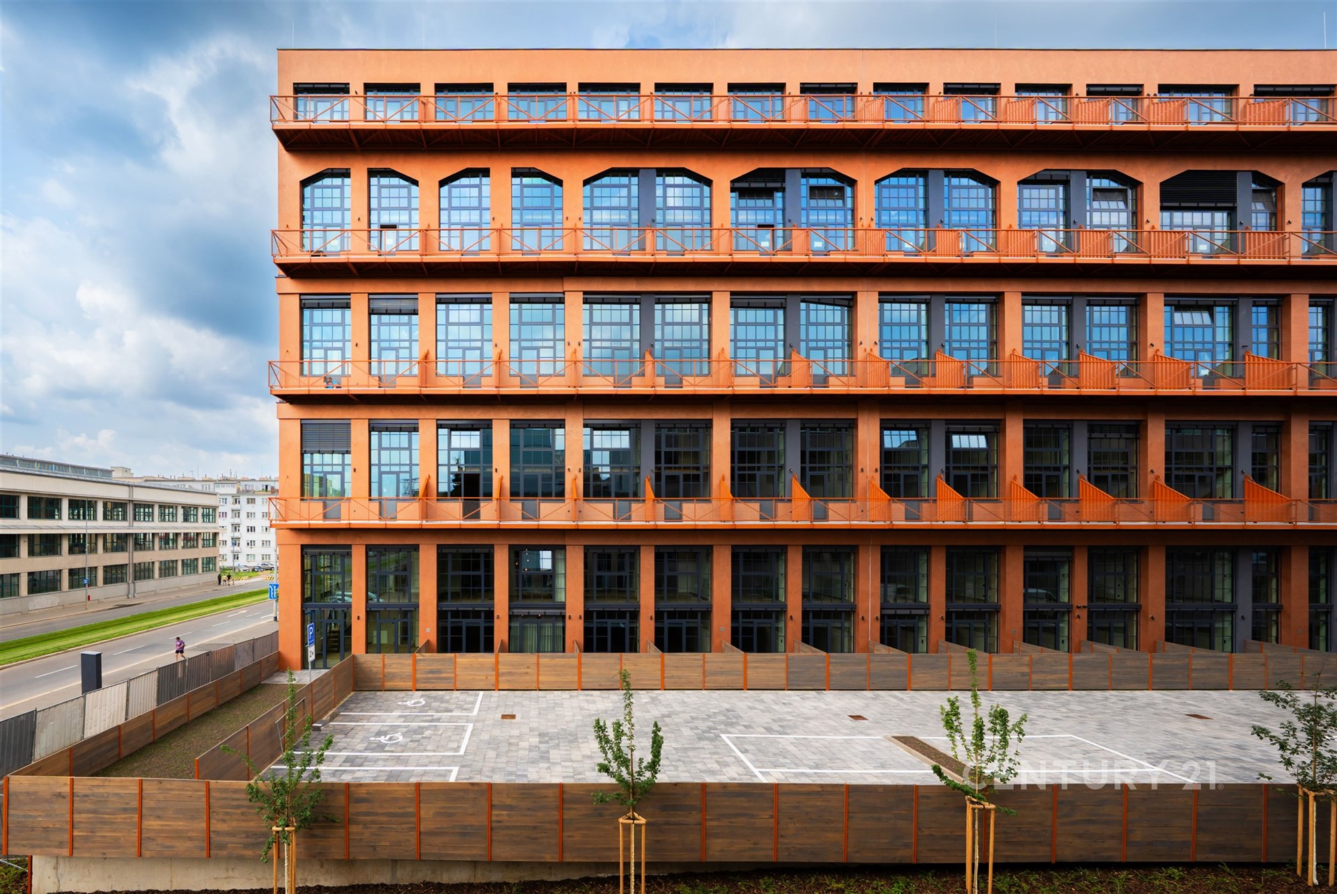 Průmyslová budova s moderními okny a cihlovou fasádou v urbanistickém stylu, okolí zahrnuje dlážděné parkoviště, současný architektonický design.