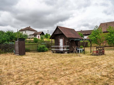 Zahrada s dřevěnými zahradními domky, obklopená plotem, s několika mladými stromy a suchým travnatým povrchem, vhodná pro rekreační účely. | Prodej - pozemek pro bydlení, 1 139 m²