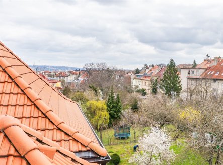 Výhled z podkrovního bytu na klidnou rezidenční čtvrť s červenými střechami, zahradami a stromovou zelení, ideální pro rodiny hledající příjemné prostředí. | Prodej bytu, 2+kk, 54 m²