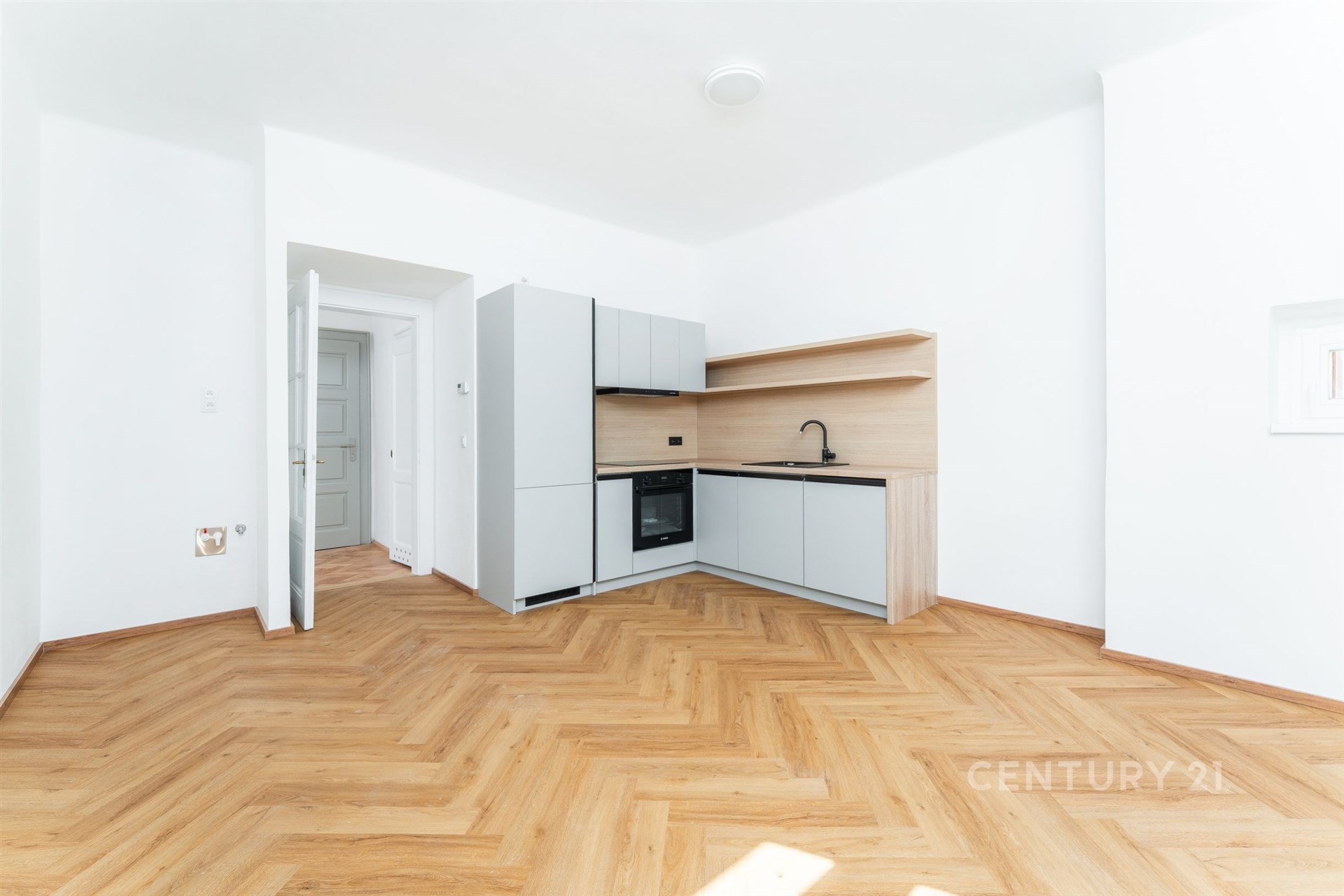 Světlá kuchyň s moderními spotřebiči, světlá parketová podlaha a minimalistický design, prostorný a vzdušný interiér.