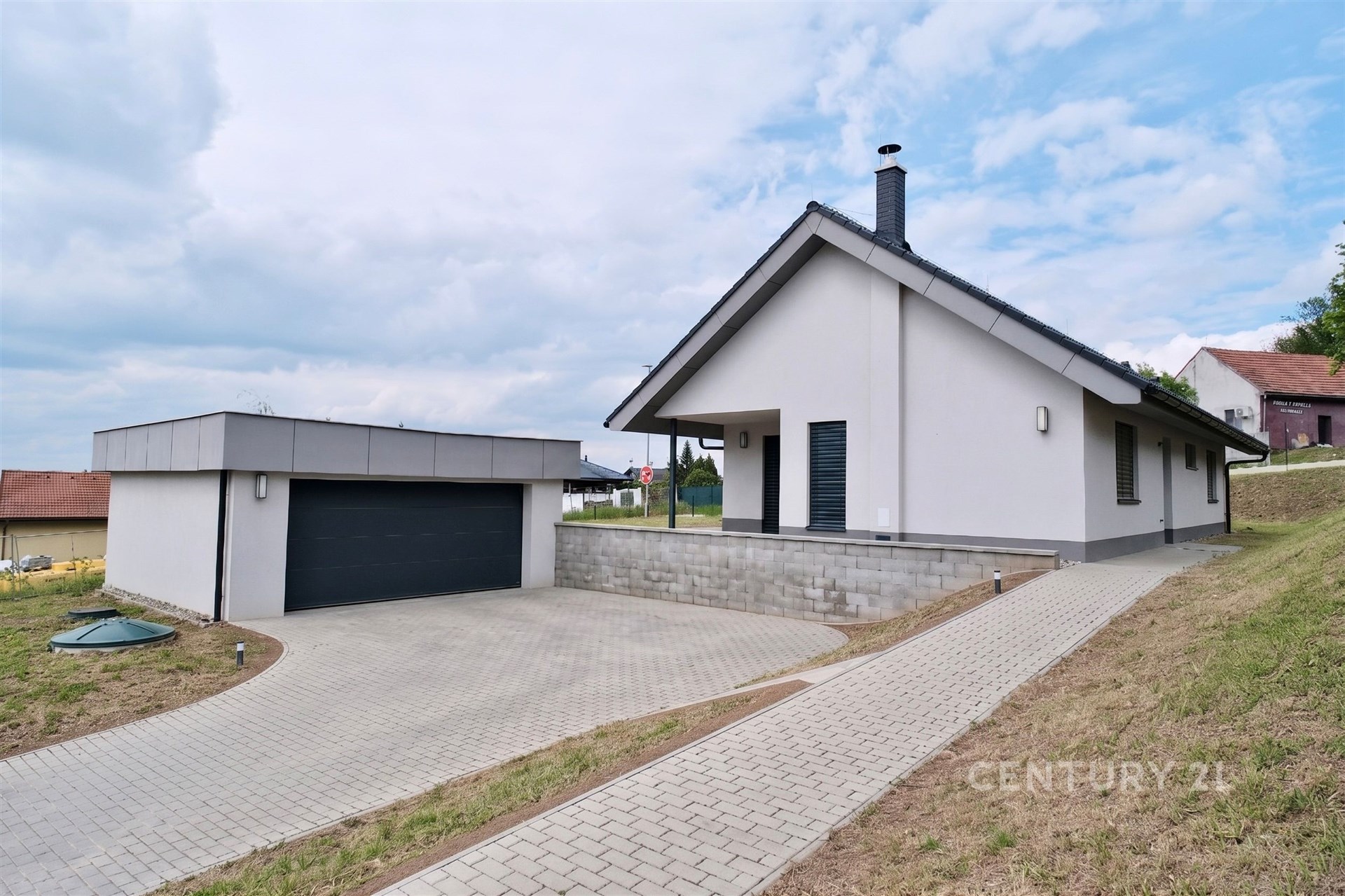 Moderní rodinný dům s dlažbou na příjezdové cestě, bílá fasáda, dvougaráž a klidná lokalita, ideální pro rodinné bydlení.