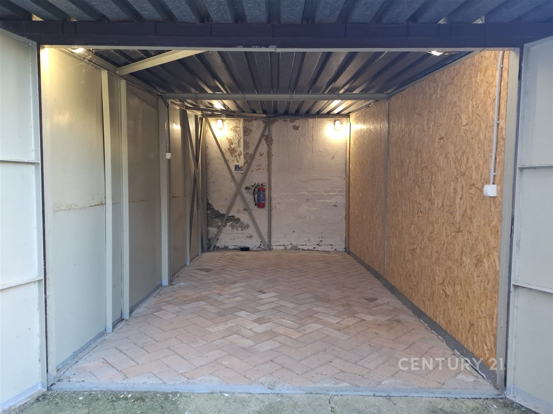 Jednoduchá garáž s průmyslovým stropem, dlážděnou podlahou a dřevěnými obklady, vhodná pro uskladnění nebo parkování vozu.