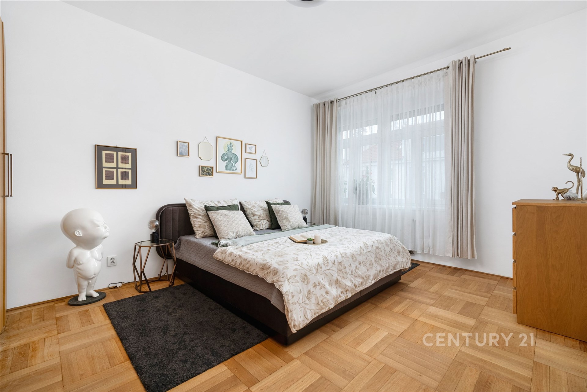 Prostorná ložnice s parketovou podlahou, velká okna zajišťující světlé prostředí, moderní nábytek, elegantní dekorace na stěnách.