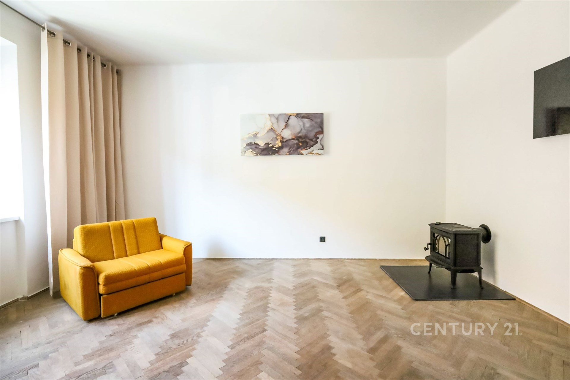 Světlý obývací pokoj s parketovou podlahou, krbová kamna dodávají útulnost, moderní minimalistický design a velké okno pro přirozené světlo