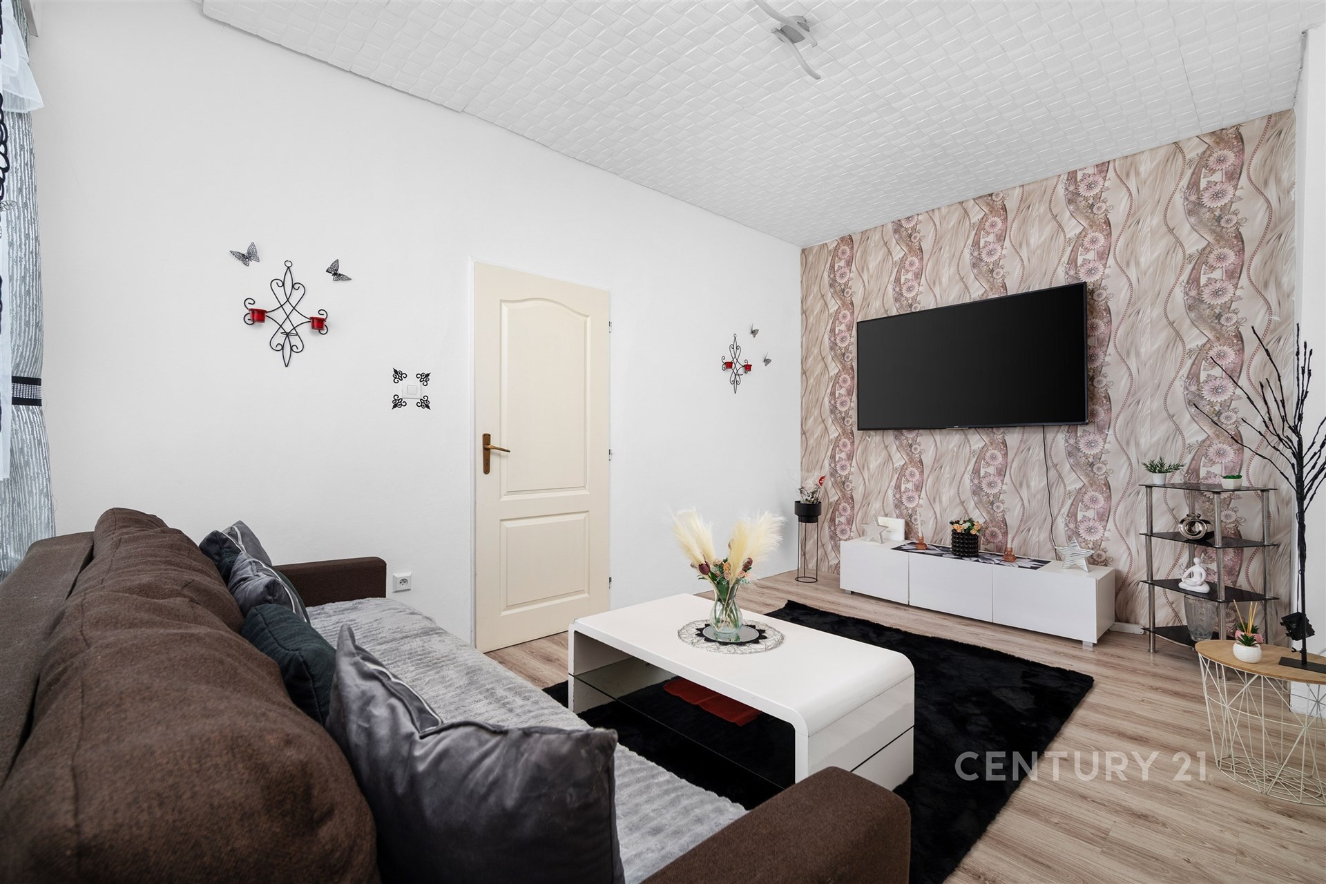 Světlý obývací pokoj s moderní dřevěnou podlahou, velkou televizí na zdi a stylovým nábytkem, ideální pro pohodlné bydlení