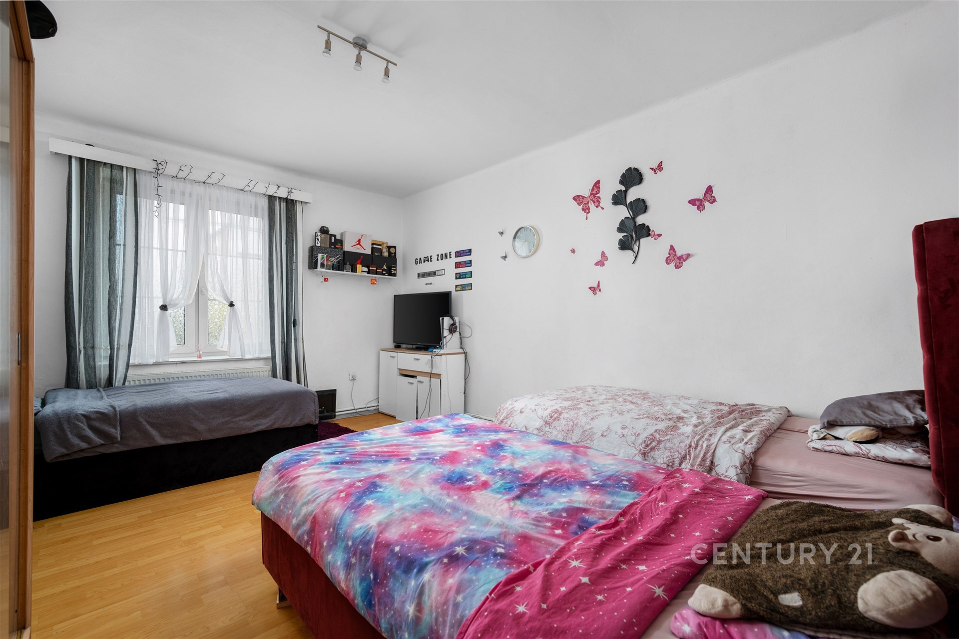 Světlá ložnice s parketovou podlahou, velkými okny a moderním nábytkem, ideální pro pohodlné bydlení.