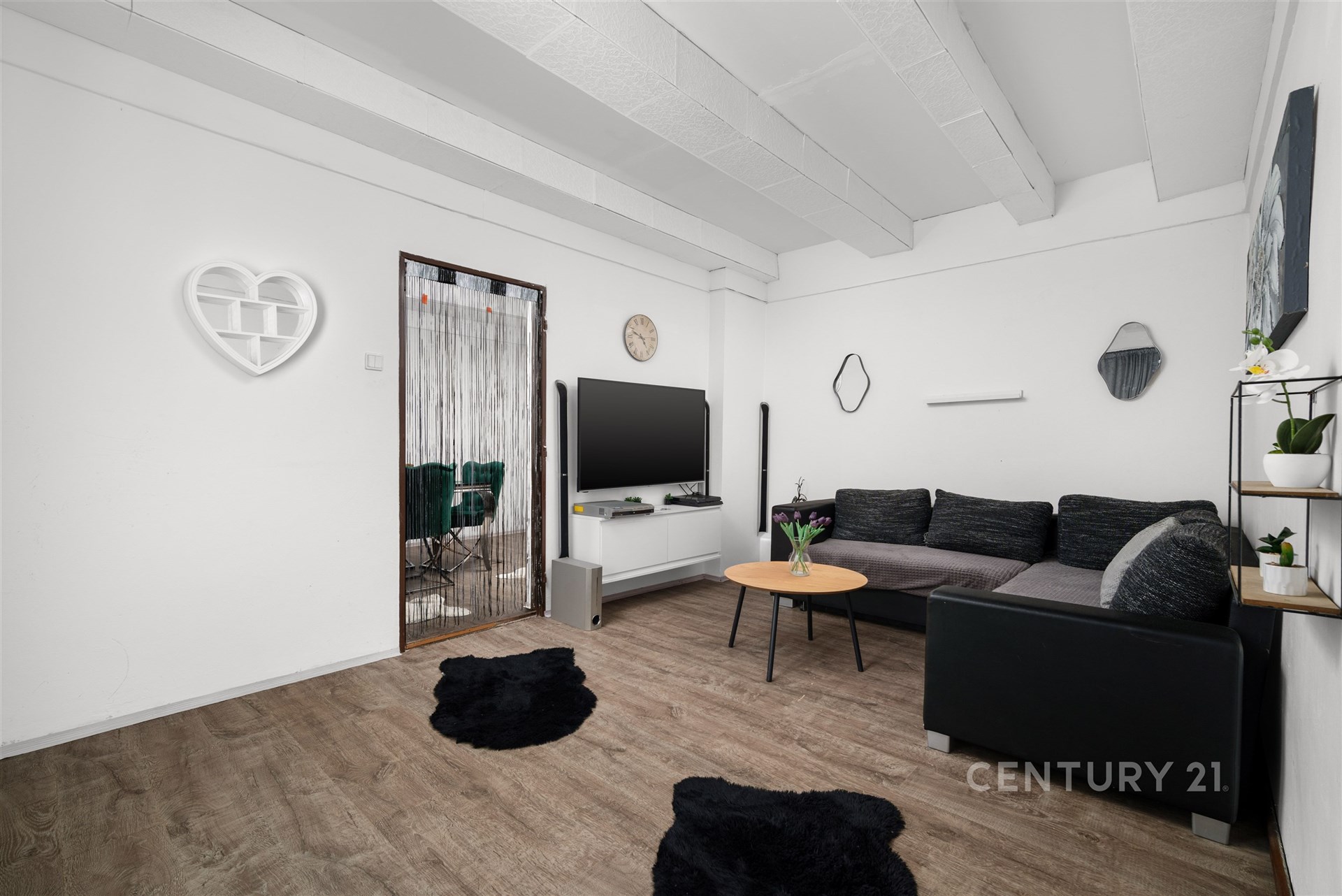 Světlý obývací pokoj s moderním nábytkem, parketovou podlahou a dekorativními prvky. Velká pohovka nabízí komfortní posezení.