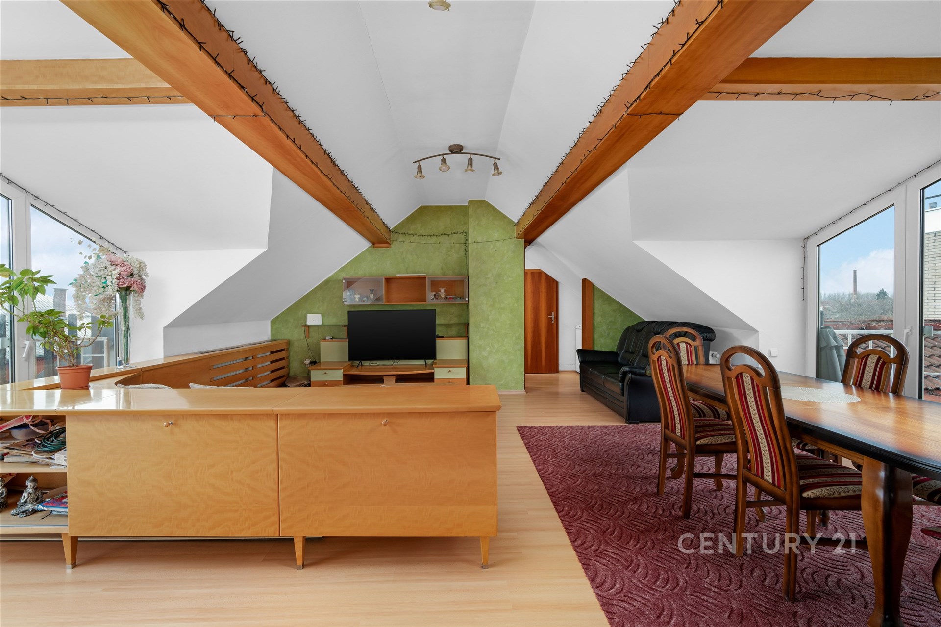 Prostorný obývací pokoj s parketovou podlahou, velkými okny a dřevěnými detaily, nabízí moderní a světlé prostředí pro pohodlné bydlení.