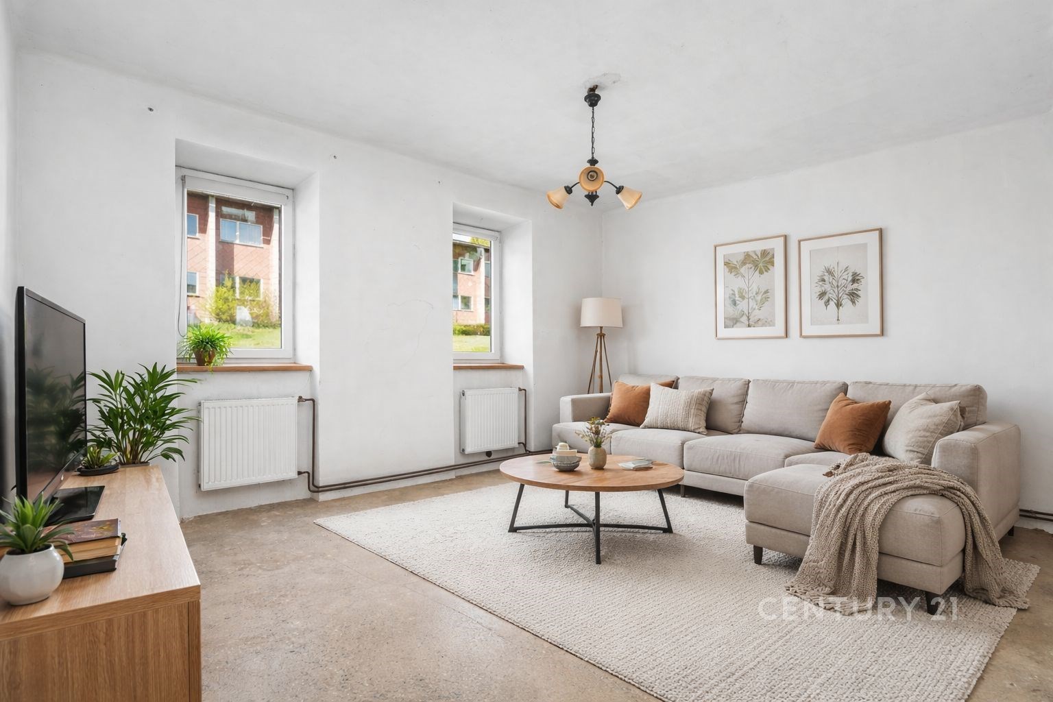 Světlý obývací pokoj s moderními betonovými podlahami, velkými okny a světlým nábytkem, vytvářejícími příjemnou atmosféru.