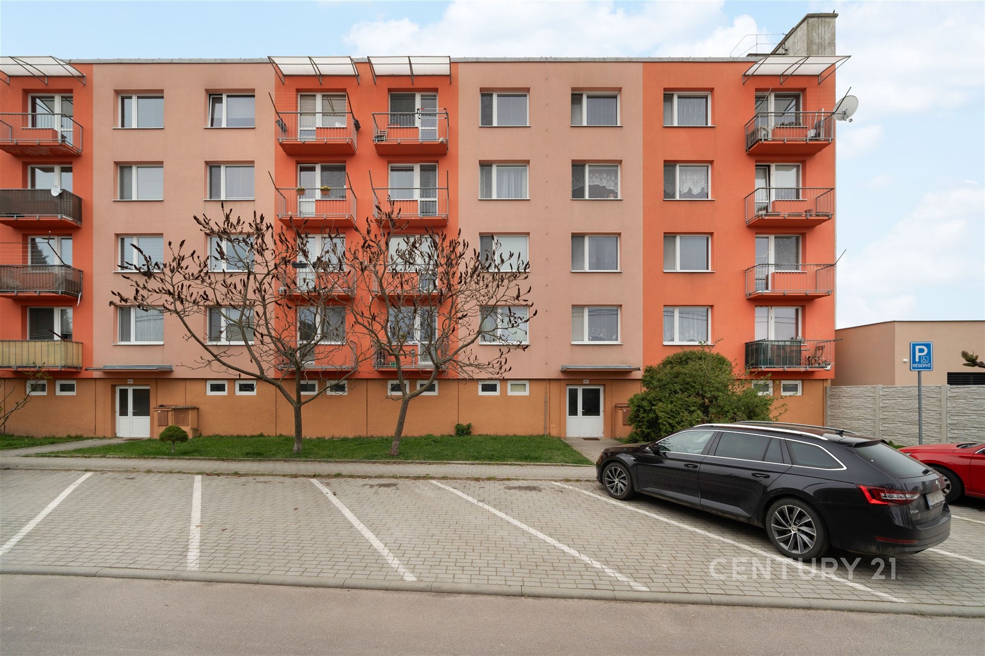 Fasáda bytového domu s balkony, parkovací místa před budovou, zateplení a moderní okna.