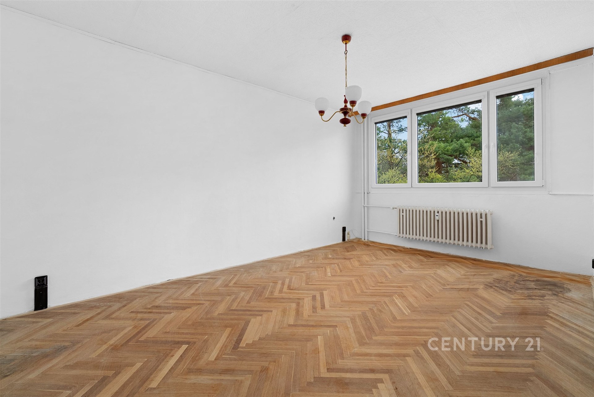 Světlý obývací pokoj s parketovou podlahou, velká okna, výhled do zeleně, vhodné pro moderní rekonstrukci.