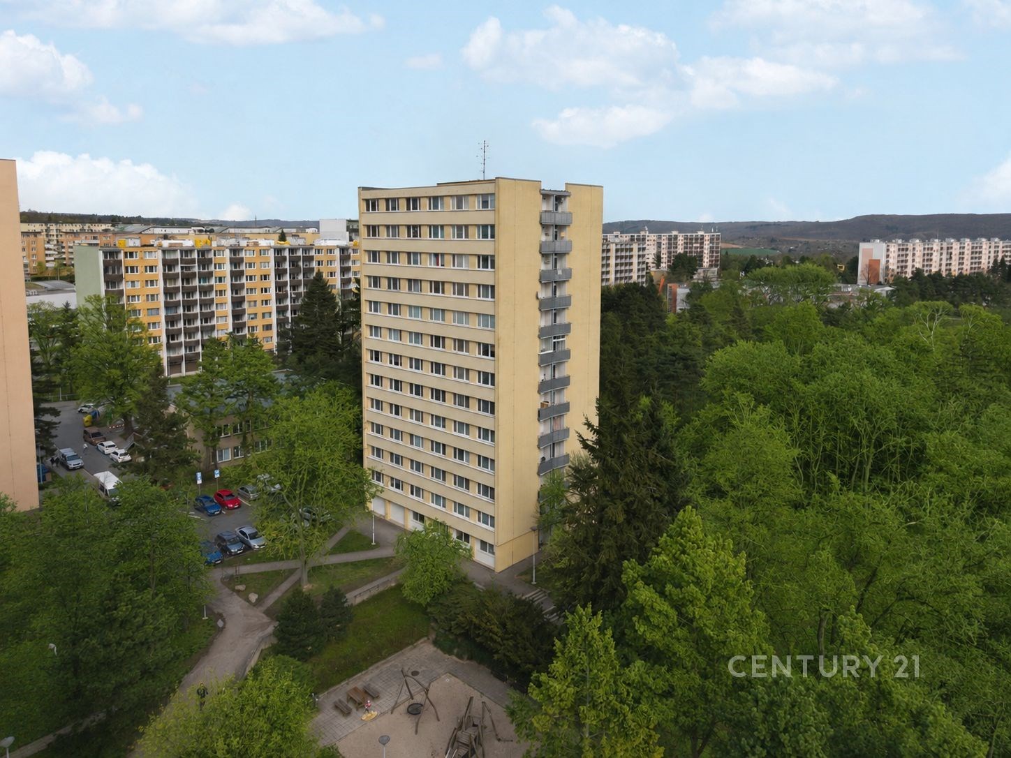 Vysoký bytový dům obklopený zelení, panelová konstrukce, dobře udržovaný, nachází se v klidné části města.