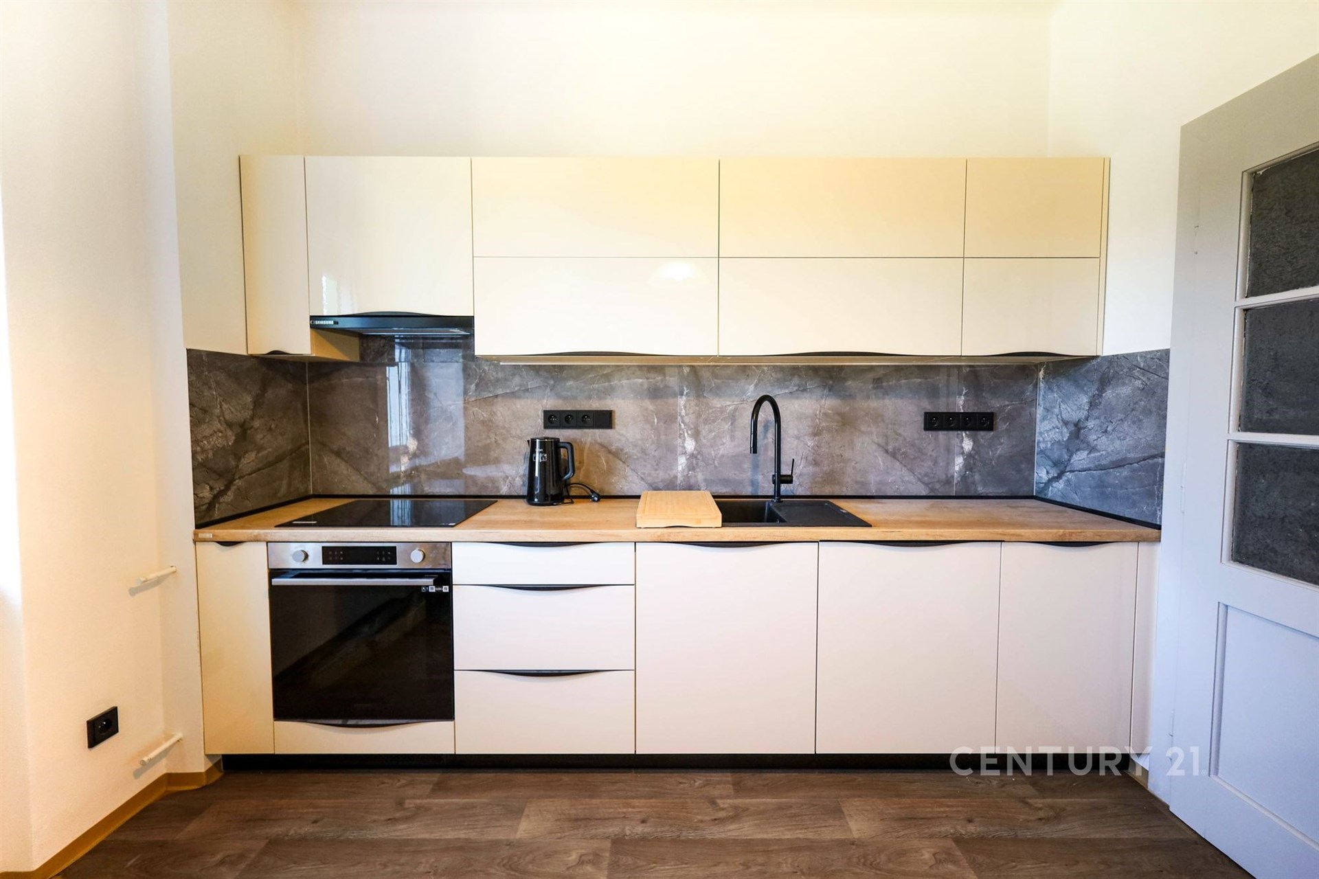 Moderní kuchyň s parketovou podlahou, vestavěnými skříněmi a elegantními spotřebiči, přináší stylové a funkční řešení pro domácnost.