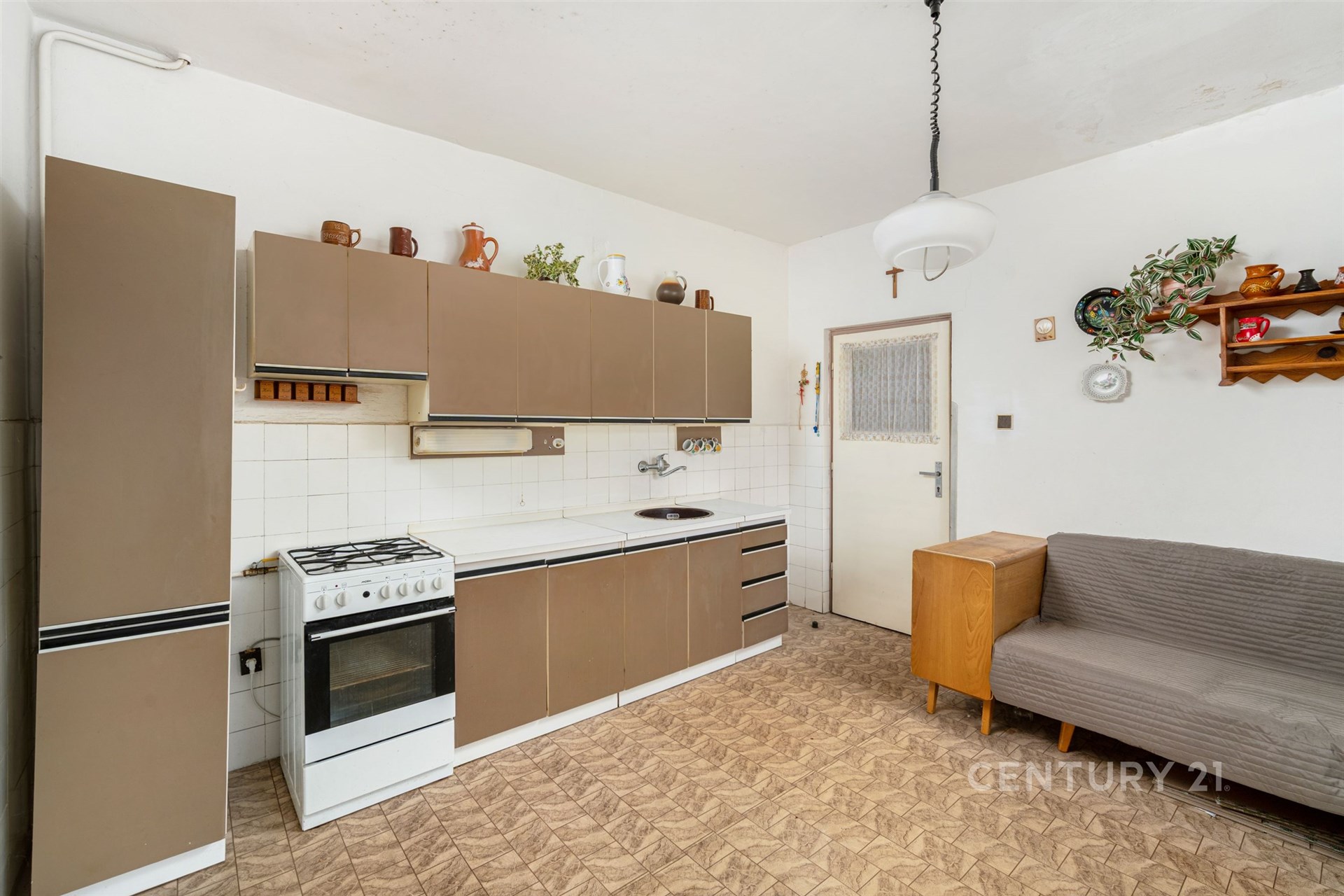 Kuchyňská linka s dlažbou a vestavěnými skříněmi, vedle gauče. Světlý prostor nabízí vintage design a praktické uspořádání.