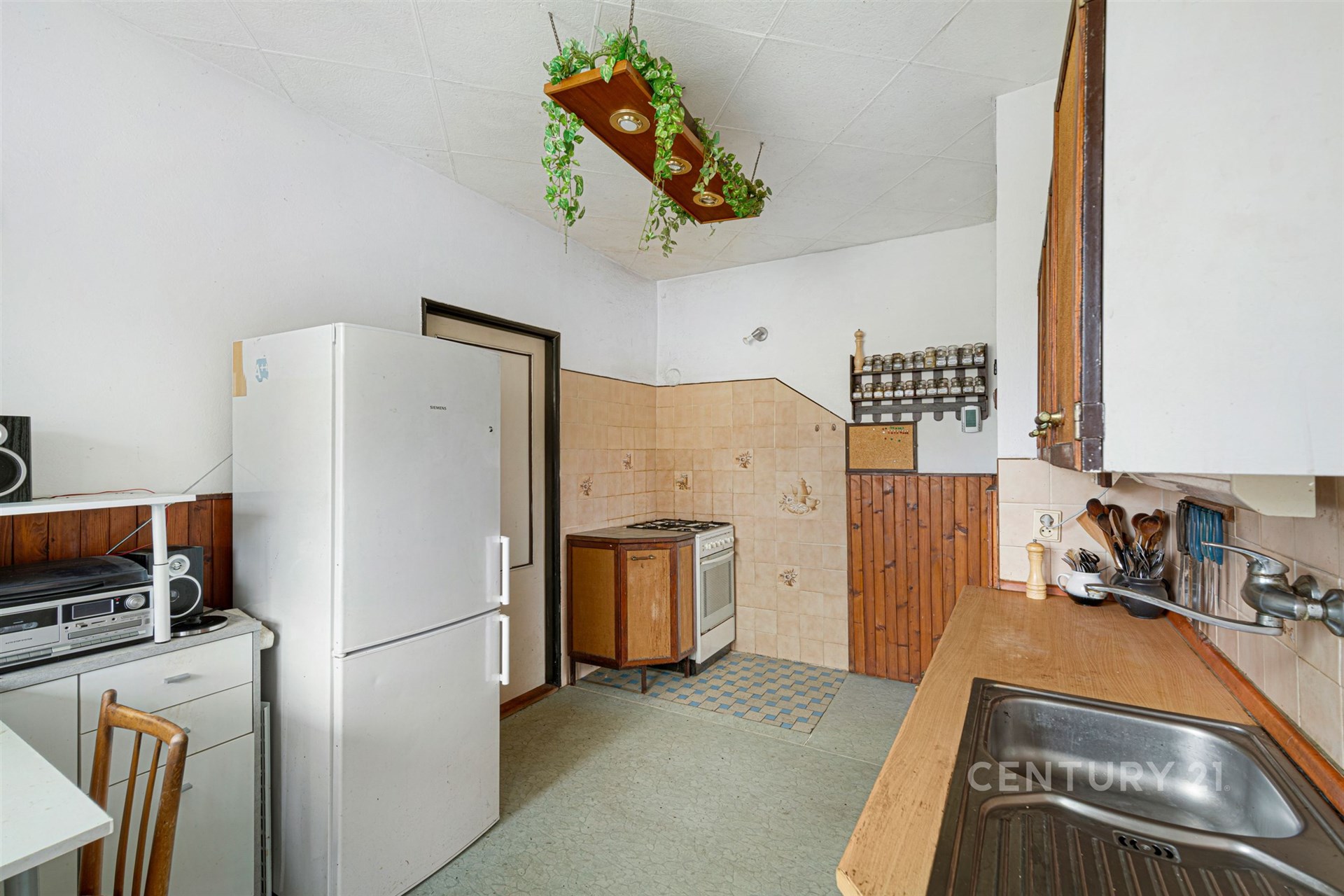 Kuchyň s retro dlažbou, dřevěným obložením a plynovým sporákem, vybavená lednicí a vestavěnými skříněmi, nabízí útulné bydlení.