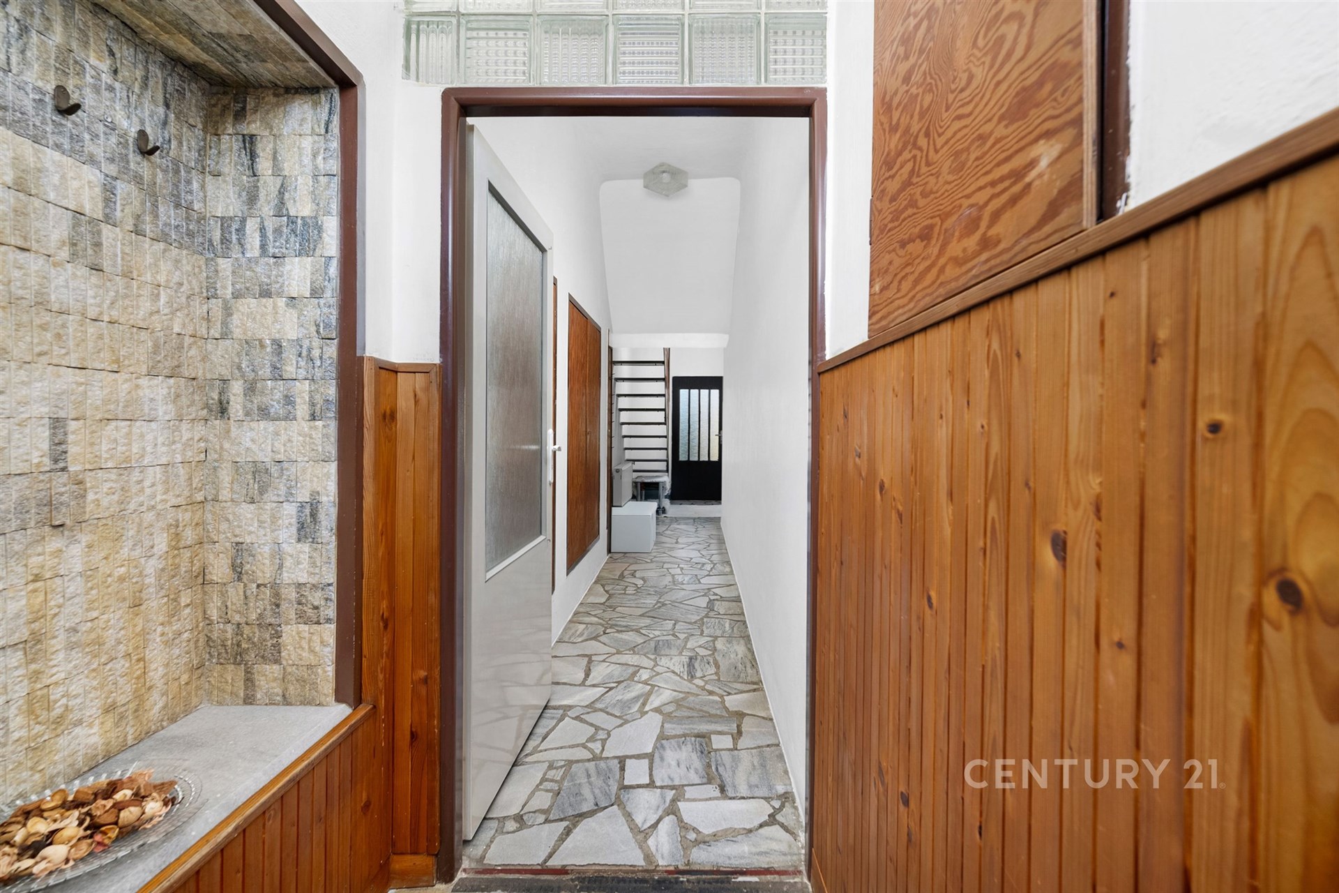 Úzká vstupní chodba s dřevěným obložením a kamennou dlažbou, moderní design, světlé stěny, skleněné dveře vedoucí do další místnosti.