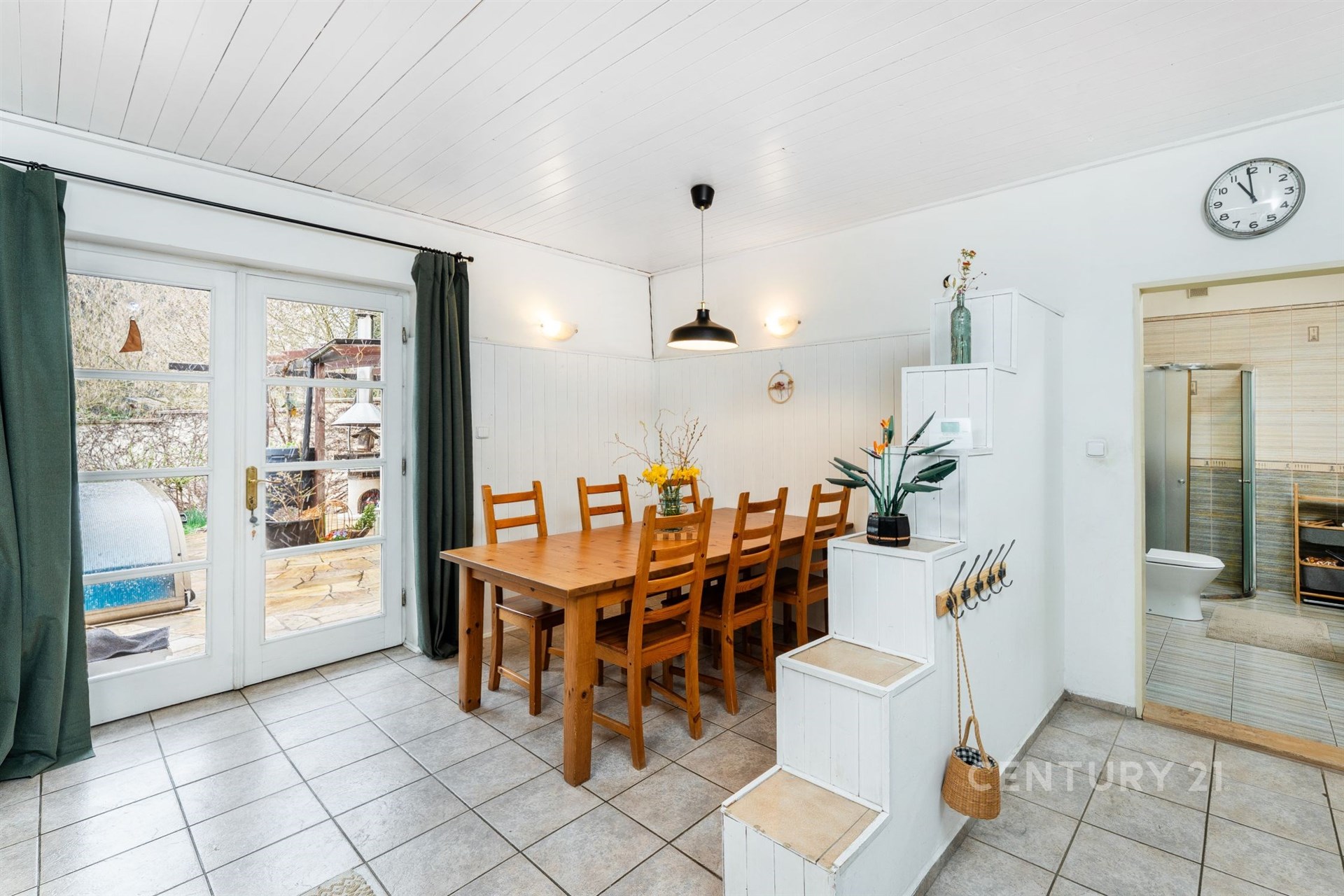 Jídelna s dlažbou, velkými okny a moderním osvětlením. Světlý prostor nabízí přístup na terasu, ideální pro rodinné večeře.