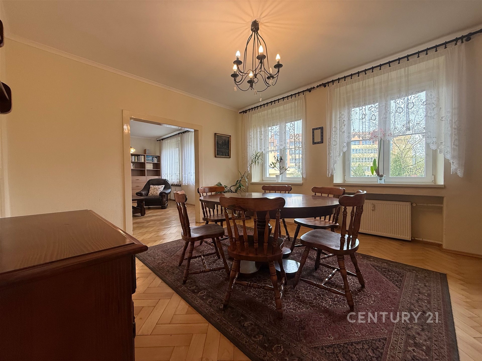 Jídelna s parketovou podlahou a velkými okny, klasický styl, dřevěný nábytek a lustr dodávají místnosti elegantní atmosféru.