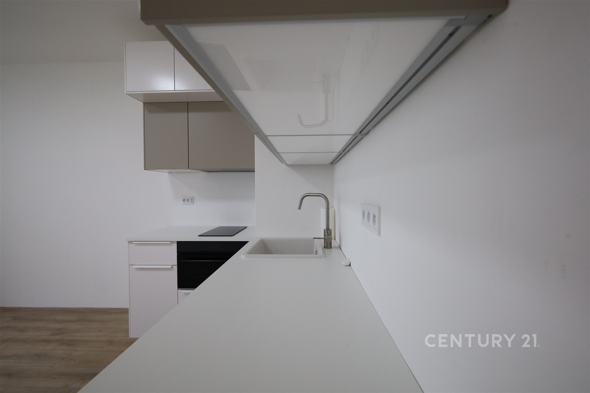 Moderní kuchyň s bílými skříňkami, vestavěnou troubou a dřezem, parketová podlaha ladí s minimalistickým designem.