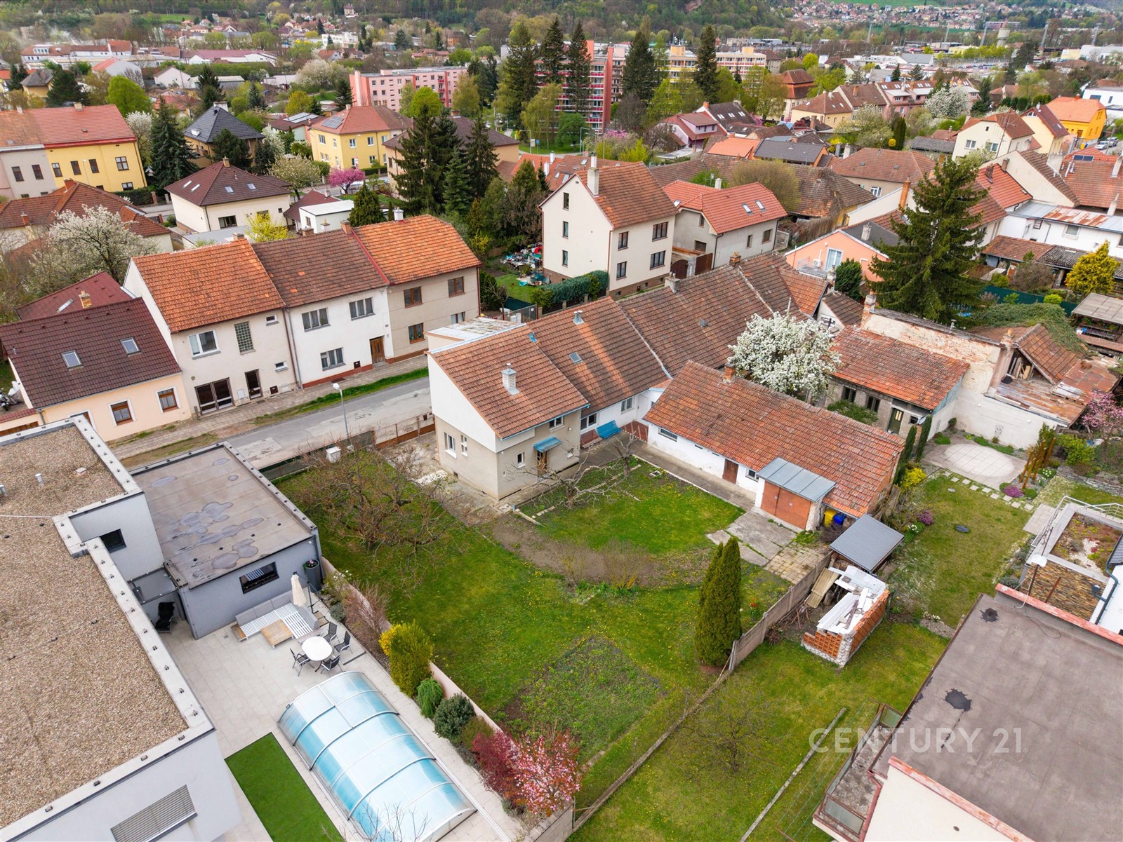 Prostorná zahrada s travnatou plochou a terasou, obklopená rodinnými domy, ve vilové čtvrti.