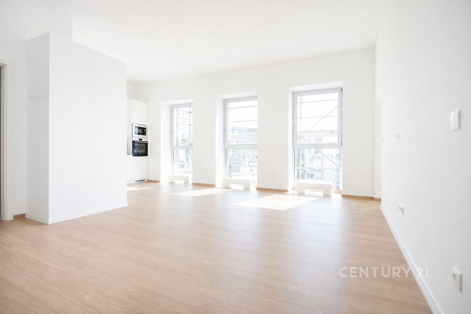 Světlý obývací pokoj s parketovou podlahou, velká okna poskytují dostatek přirozeného světla, moderní čistý design interiéru.