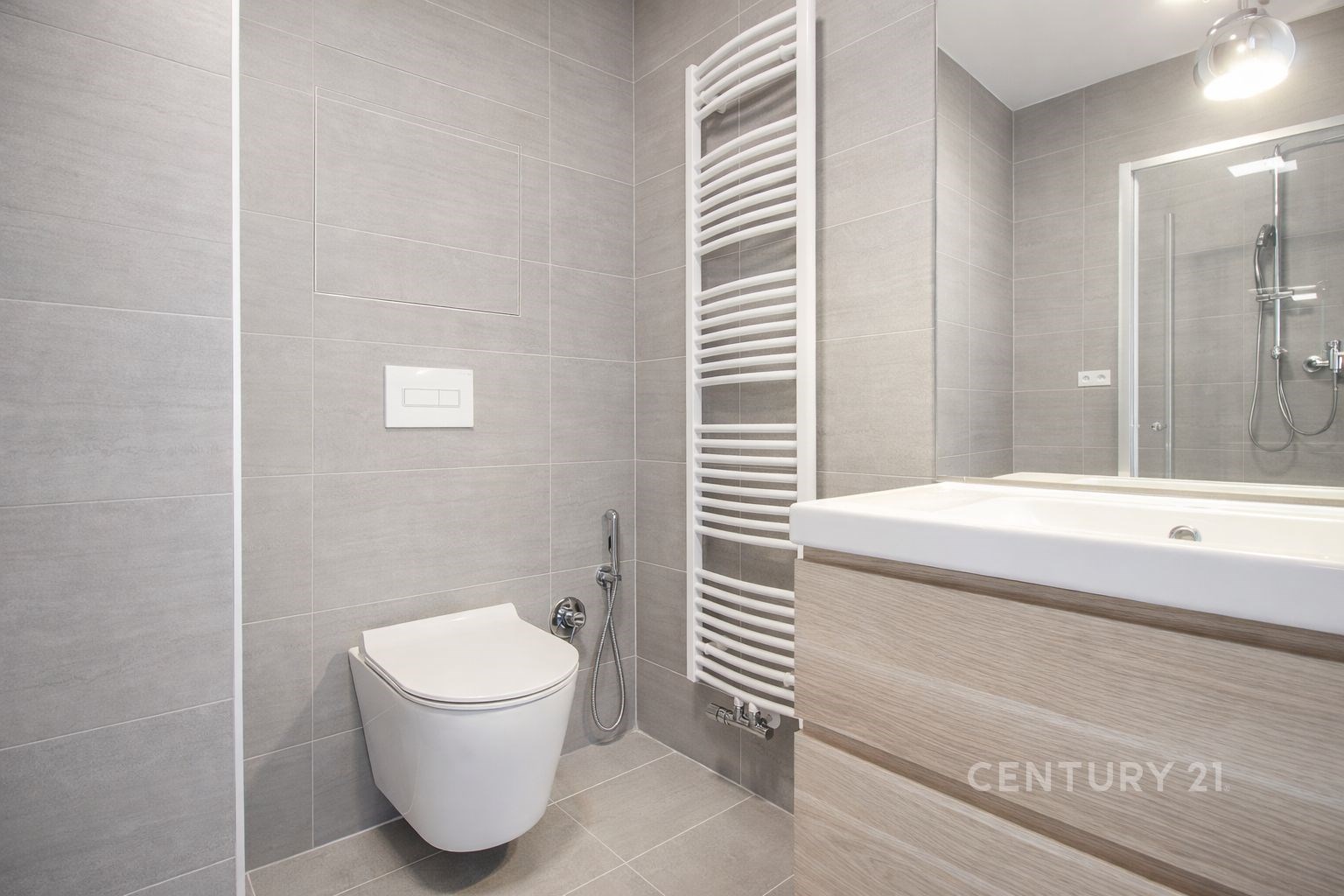 Moderní koupelna s šedou dlažbou, závěsnou toaletou a dřevěným umyvadlovým pultem, doplněná otopným žebříkem a sprchovým koutem.