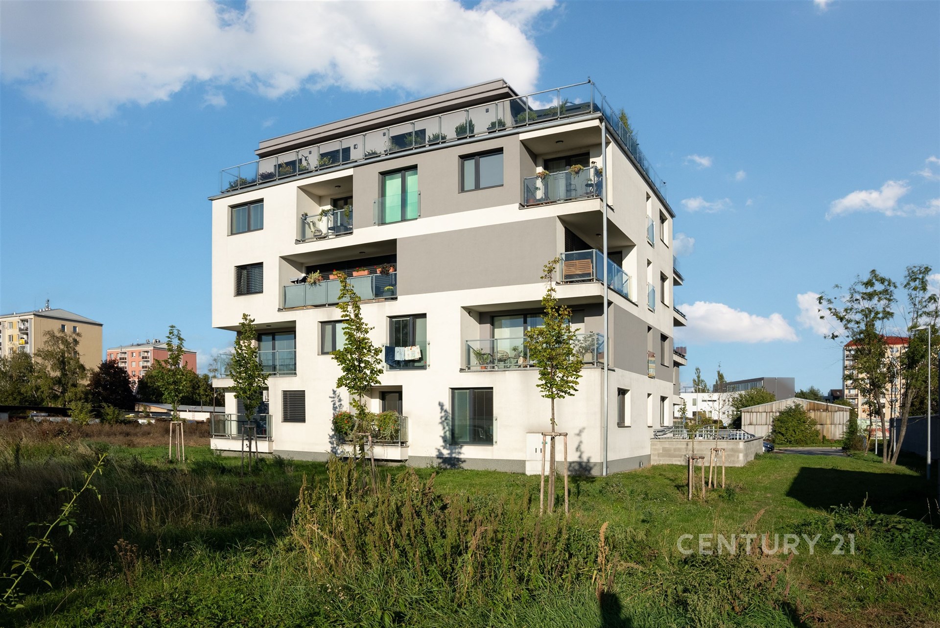 Moderní bytový dům s velkými okny a balkony, nacházející se v klidné lokalitě. Budova je novostavba s elegantním designem.