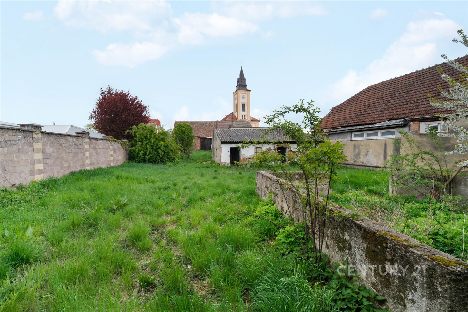 Zahrada s velkým travnatým pozemkem a výhledem na kostelní věž, obklopená kamennými zdmi, ideální pro výstavbu nebo renovaci.