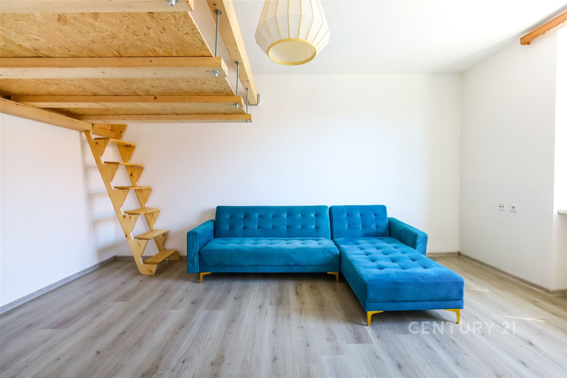 Obývací pokoj s modrou rohovou sedačkou, světlou parketovou podlahou a dřevěným schodištěm, moderní design a velká okna přinášejí dostatek světla.