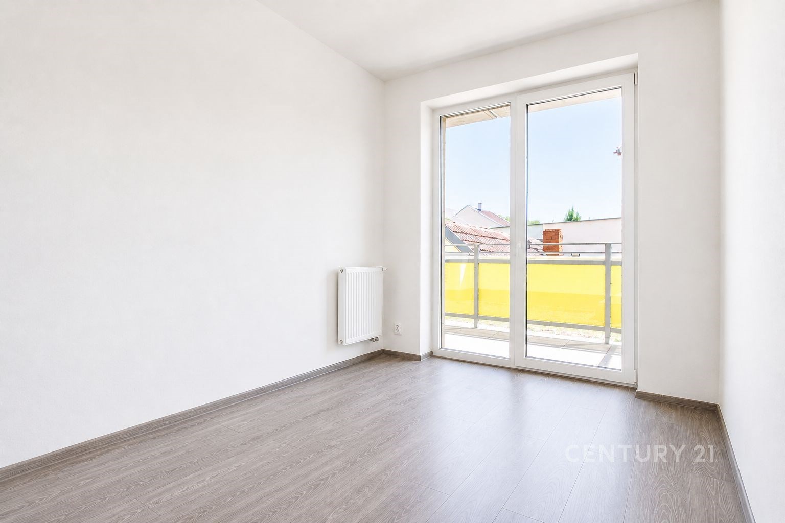 Světlý pokoj s velkými okny, moderní dlažbou a přístupem na balkon, ideální prosvětlený prostor k relaxaci.