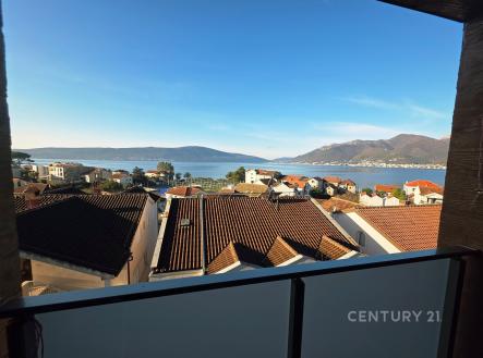 Výhled z balkonu na střechy domů, s panoramatem moře a hor. Moderní zábradlí, vynikající lokalita, ideální pro klidné bydlení.
