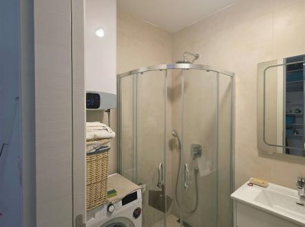 Malá koupelna s moderním sprchovým koutem, světlá dlažba a vestavěným úložným prostorem, obsahuje pračku a umyvadlo s úložným prostorem.