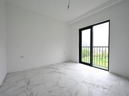 Světlá ložnice s dlažbou a velkým oknem, které poskytuje výhled do zahrady, moderní minimalistický design bez nábytku.