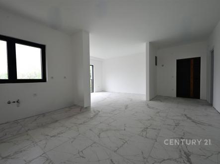 Prostorný obývací pokoj s mramorovou dlažbou, velkými okny a moderní bílou stěnou, ideální pro světlé a vzdušné bydlení.